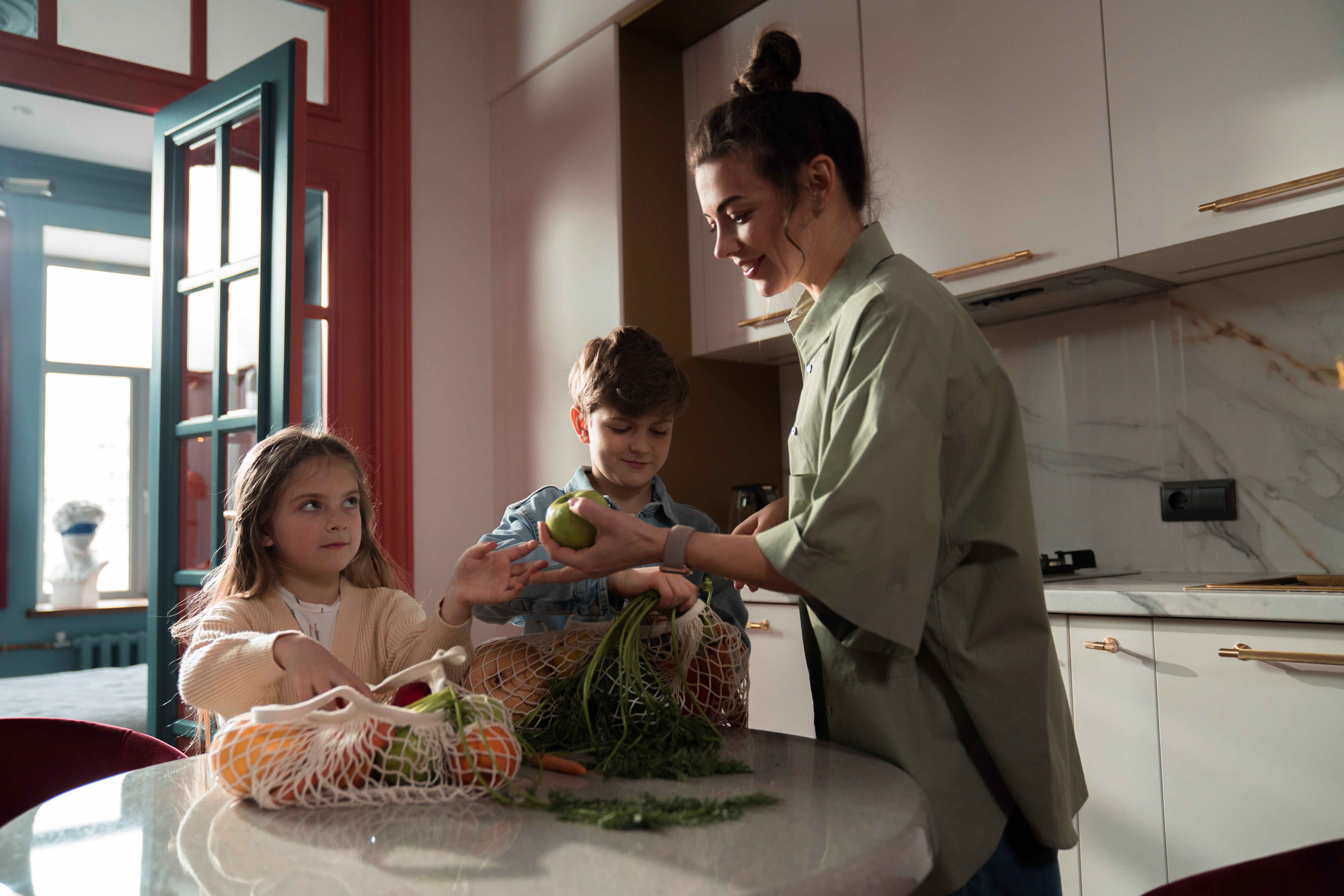 An adult and two children unpacking groceries together in a kitchen